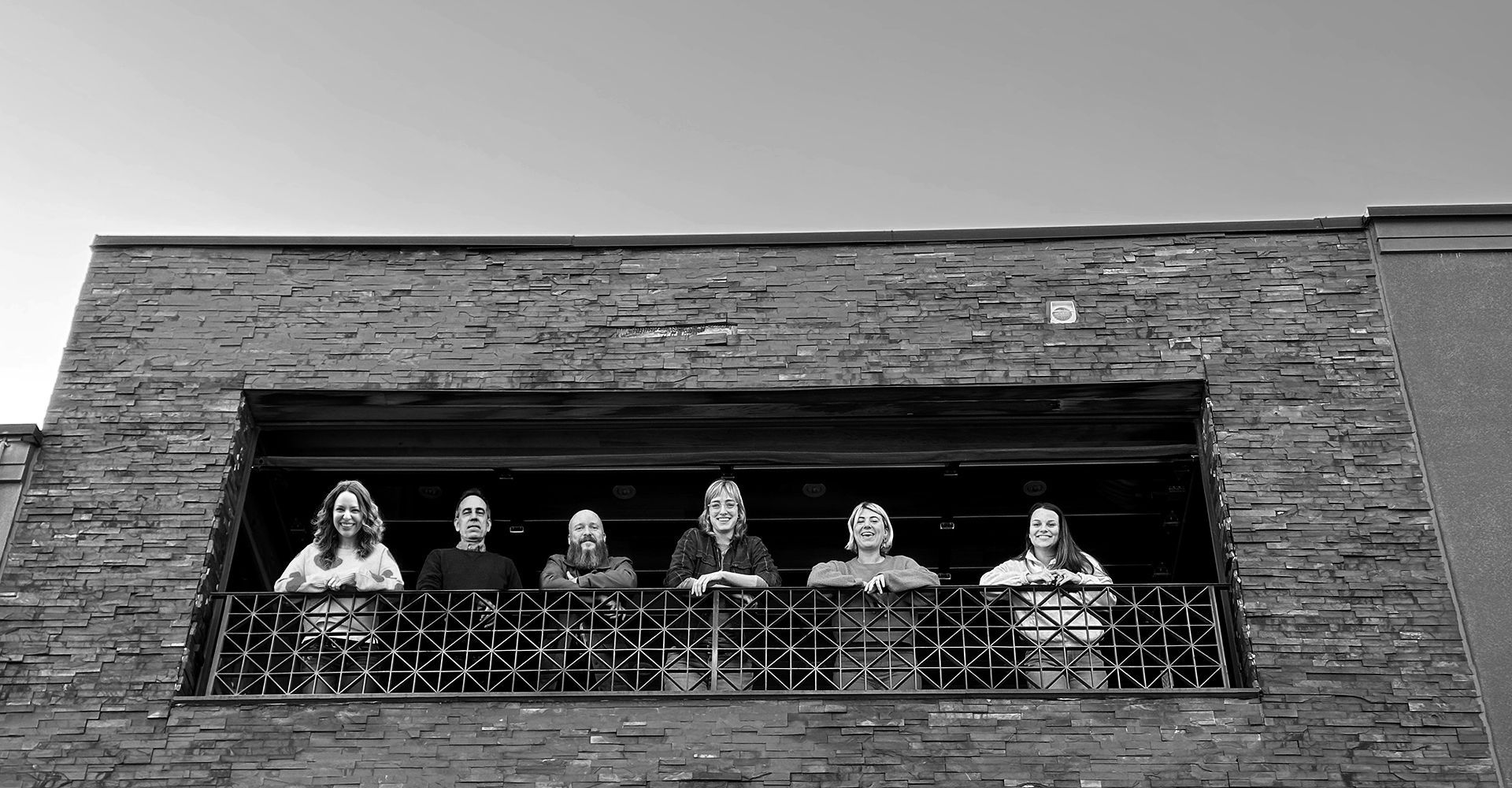A group of people are standing on a balcony in front of a brick building.