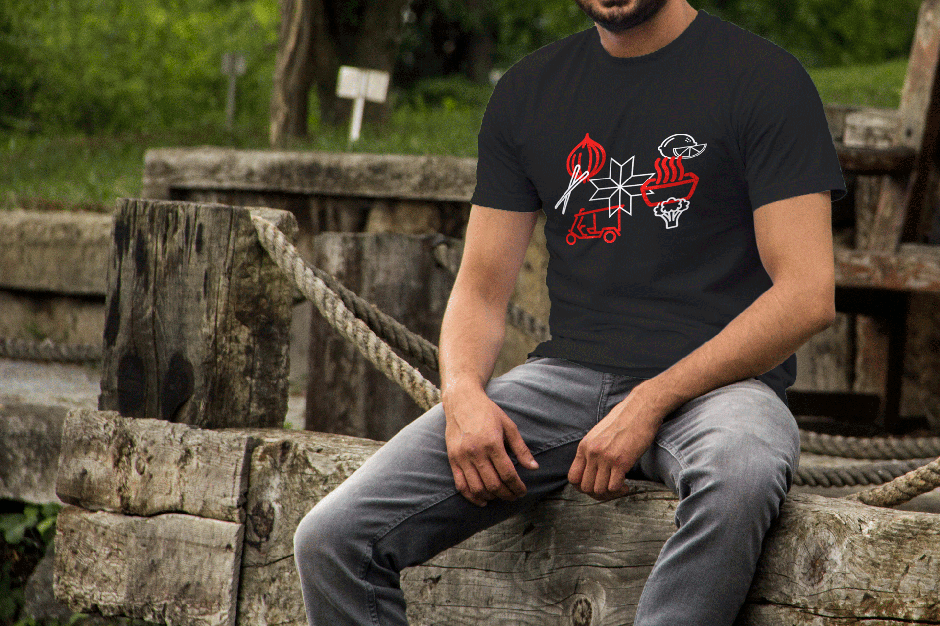 A man wearing a black t-shirt is sitting on a wooden fence.