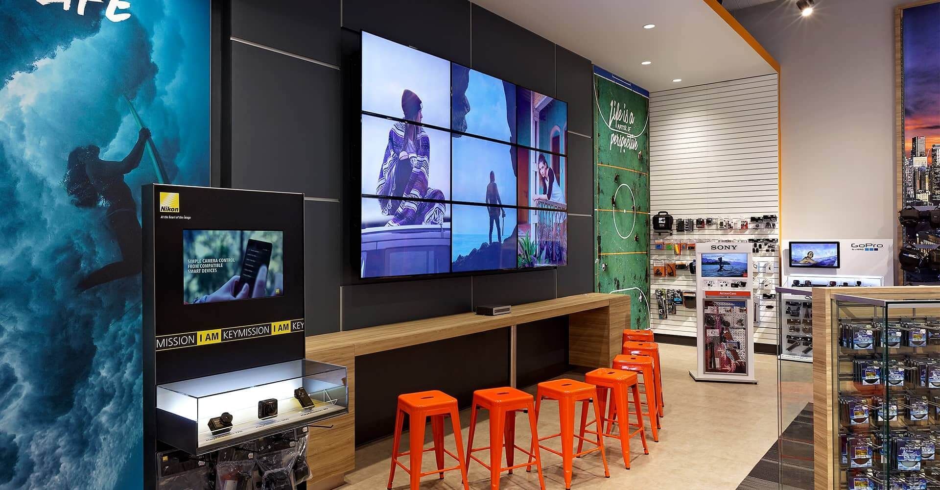 A store with a large screen on the wall and orange stools
