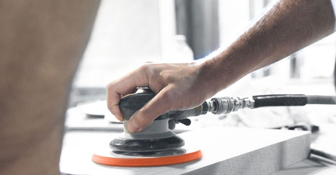 A person is sanding a piece of wood with an air sander.