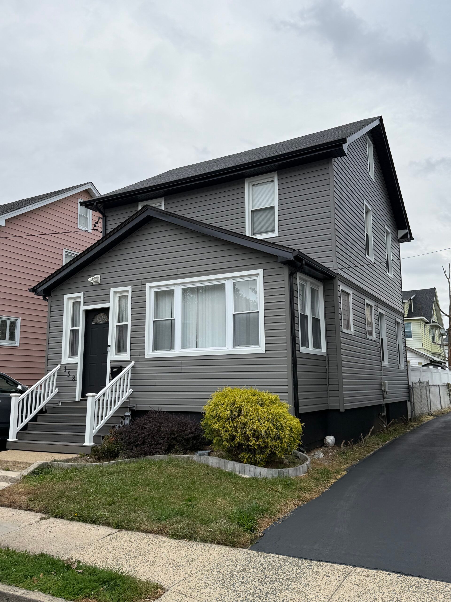 Two-story gray house with white trim, a small front yard, and a black driveway on a cloudy day.