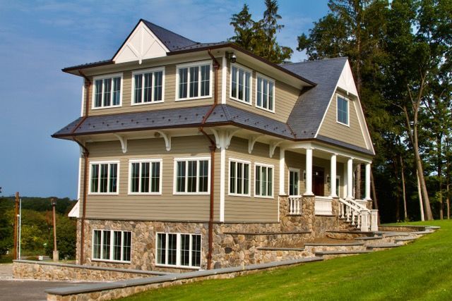 Multi-story house with green siding, stone base, and slate roof. Porch and grassy lawn.