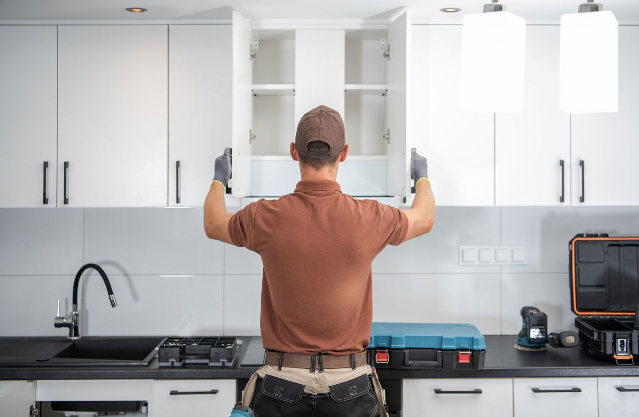 A person in work clothes opening kitchen cabinet doors.