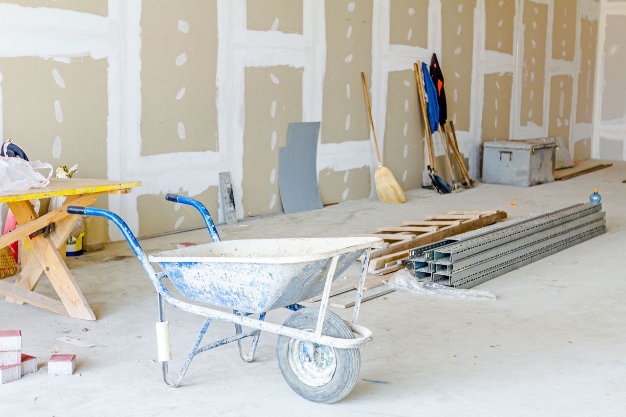 Construction site with drywall, a wheelbarrow, tools, and materials.