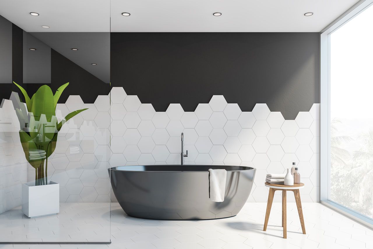 Modern bathroom with a gray soaking tub, white and black hexagon tiles, and a large window.