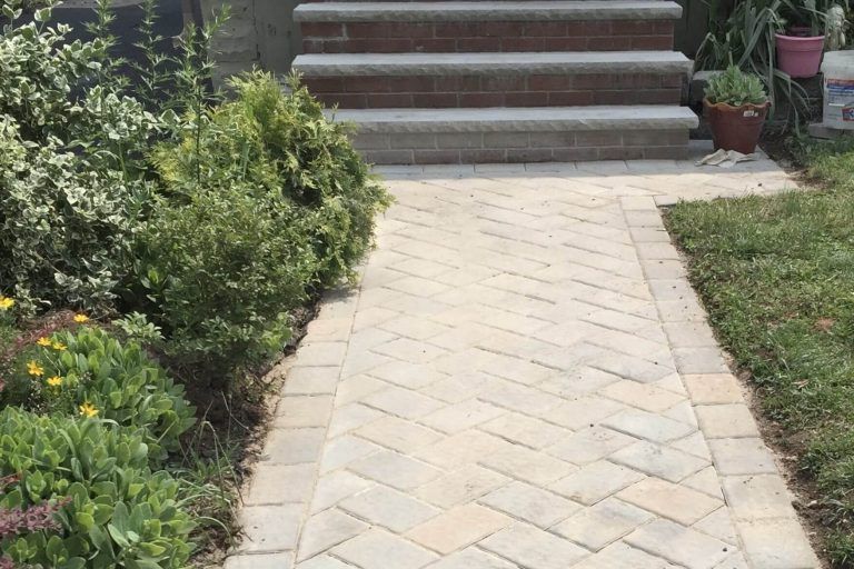 Brick pathway leading to brick steps, flanked by greenery and grass.