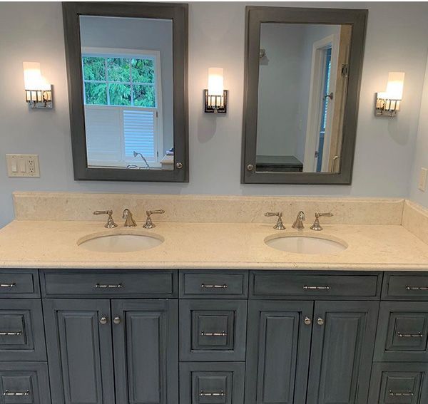 Bathroom with dual sinks, gray cabinets, beige countertop, framed mirrors, and sconce lighting.