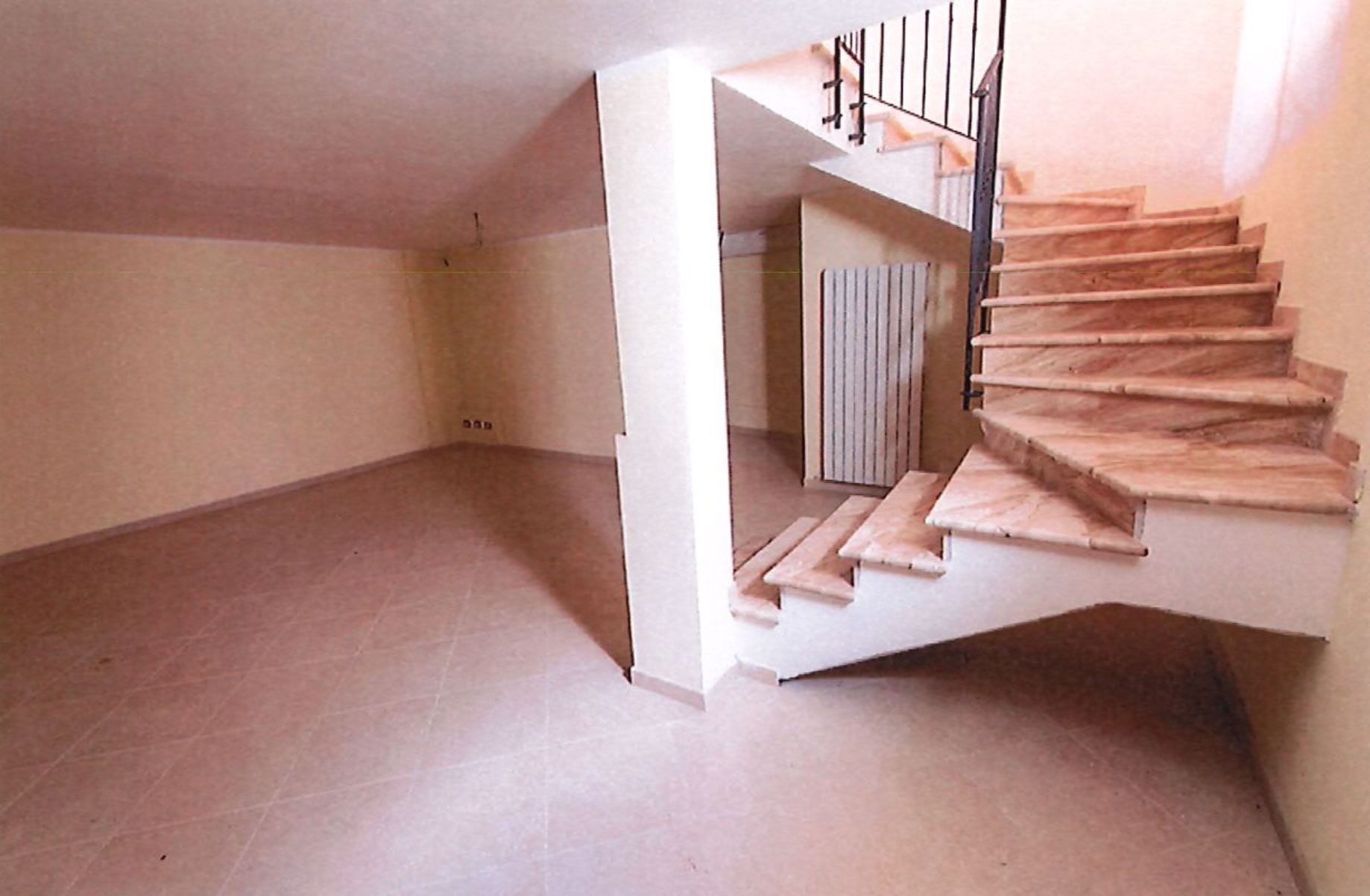 Interior view of a room with stairs. Beige walls and floor. Stairs have wooden steps, black railing.