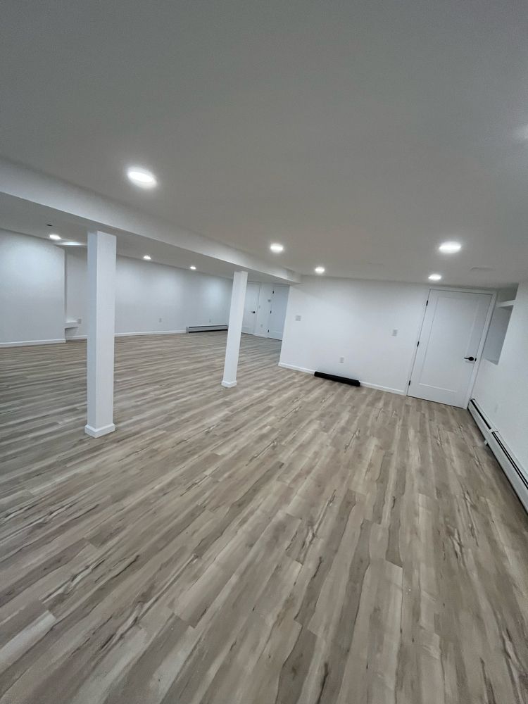 Empty, renovated basement with light gray wood-look flooring and white walls, recessed lighting.