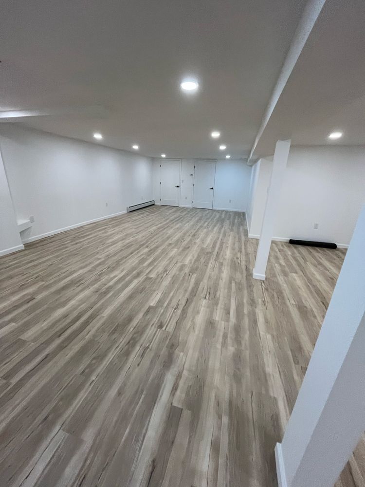 Empty, rectangular room with light gray wood-look flooring and white walls and ceiling; overhead lighting.