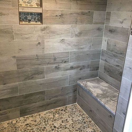 Gray tiled shower with pebble floor, built-in bench, and a small, tiled shelf.