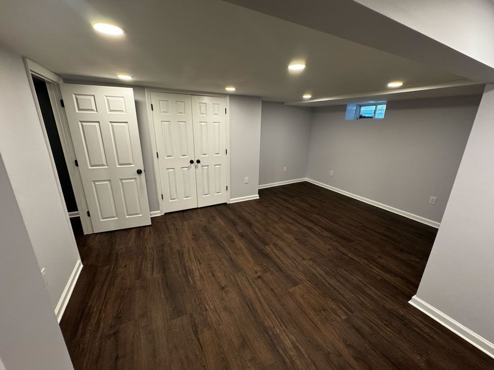 Empty, newly renovated room with dark wood-look flooring, light gray walls, white doors, and recessed lighting.