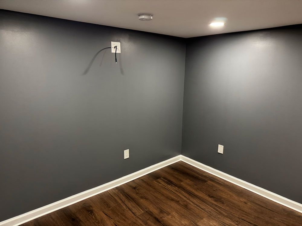 Empty room with dark gray walls, white trim, and wood-look flooring. One wall has a 