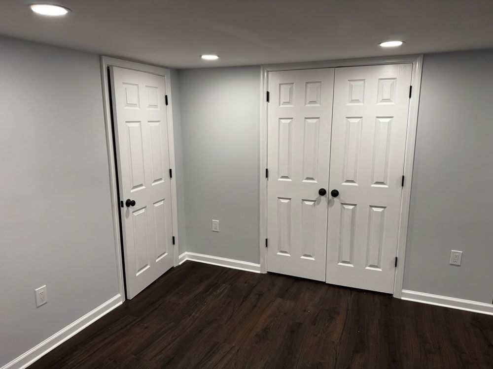 A room with two white doors, gray walls, dark wood floor, and recessed lights.