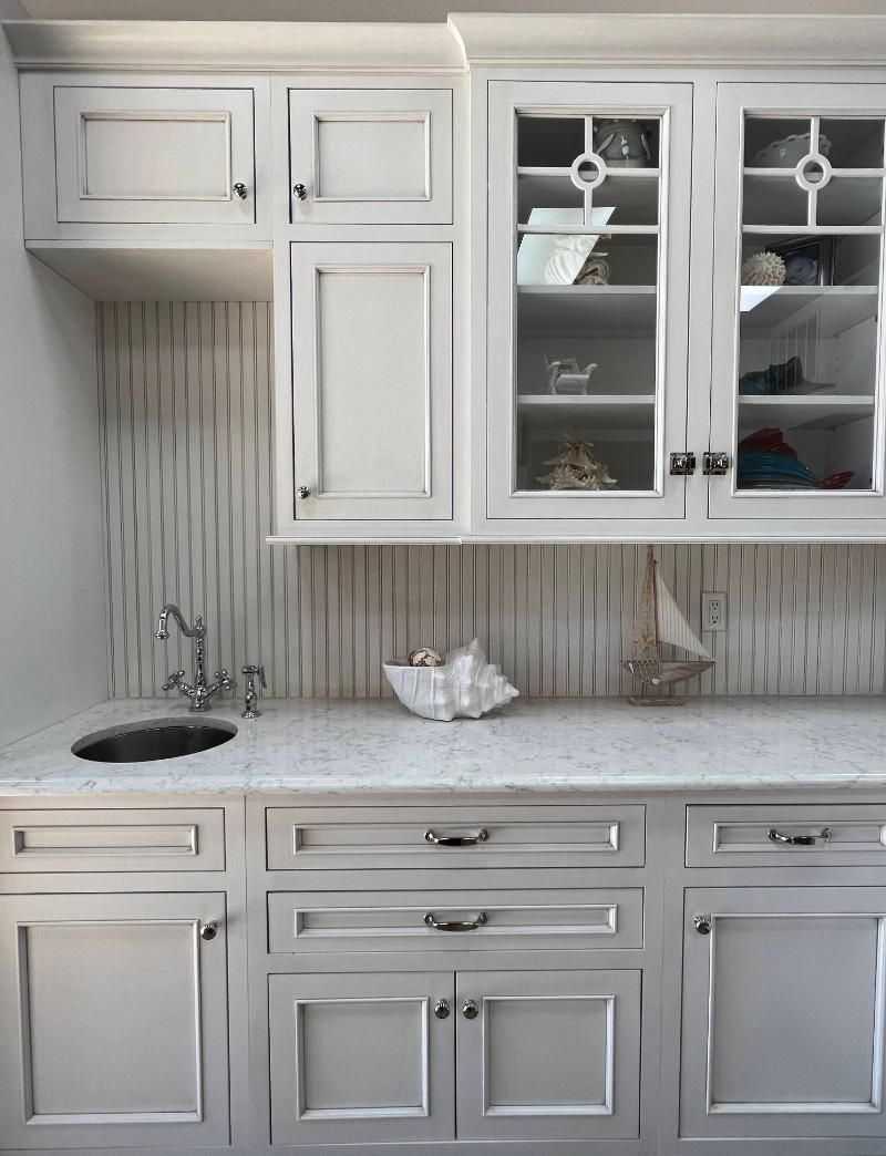 White kitchen cabinets with a marble countertop, small sink, and nautical decor.