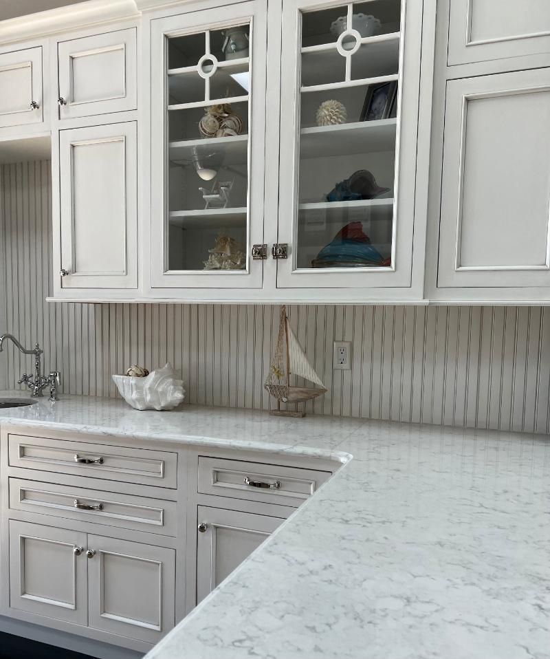 White kitchen cabinets with glass-fronted upper cabinets displaying decor, and a white countertop.