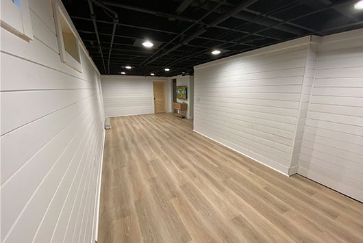 Basement with white shiplap walls, light wood-look floors, black ceiling, and recessed lighting.