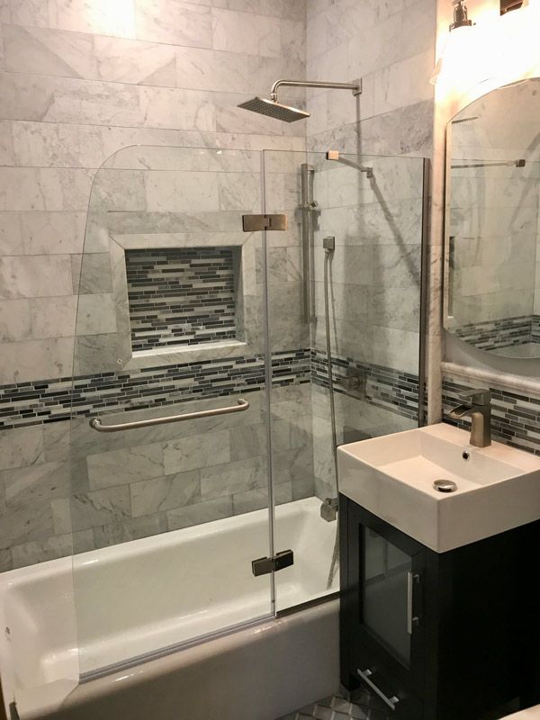 Bathroom with white bathtub, shower, glass door, and marble tile walls.
