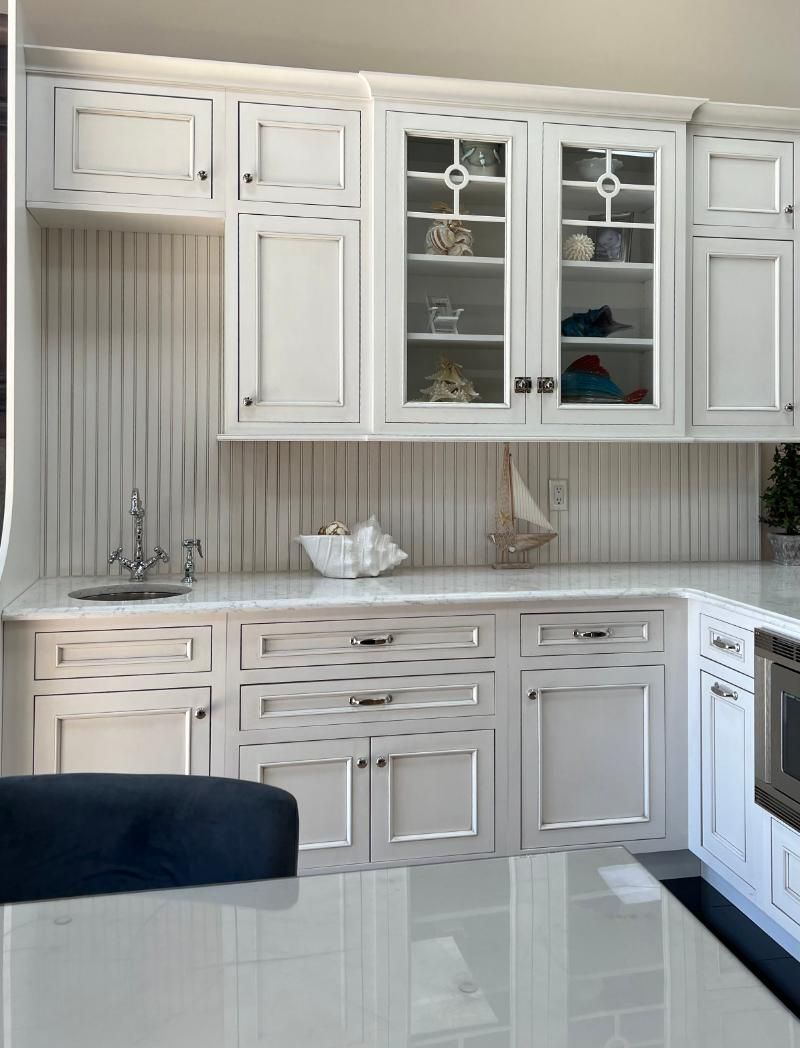 White kitchen cabinets with glass-fronted display, marble countertops, sailboat decor.