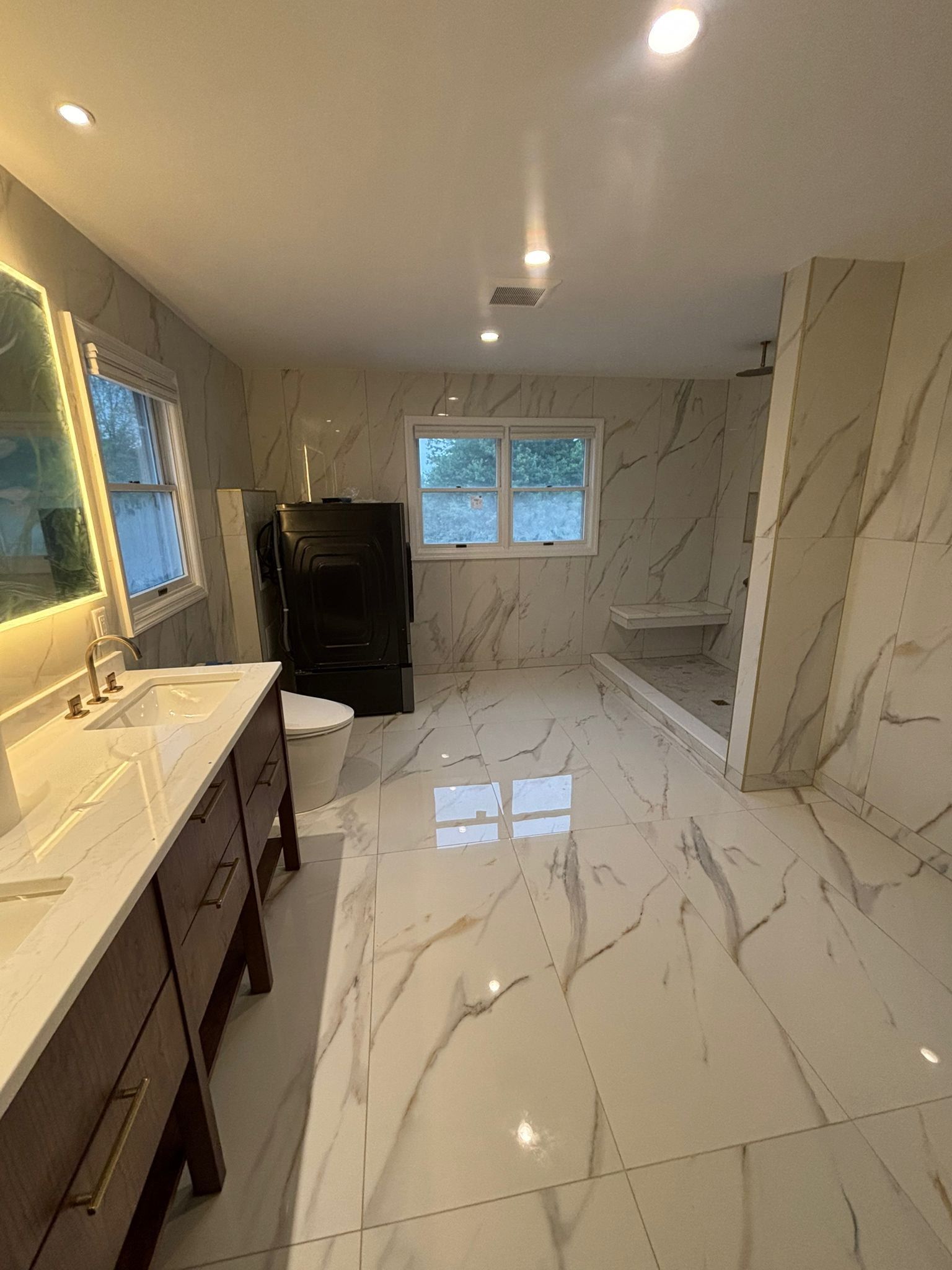 Bathroom with white marble tile, brown vanity, and black appliance.