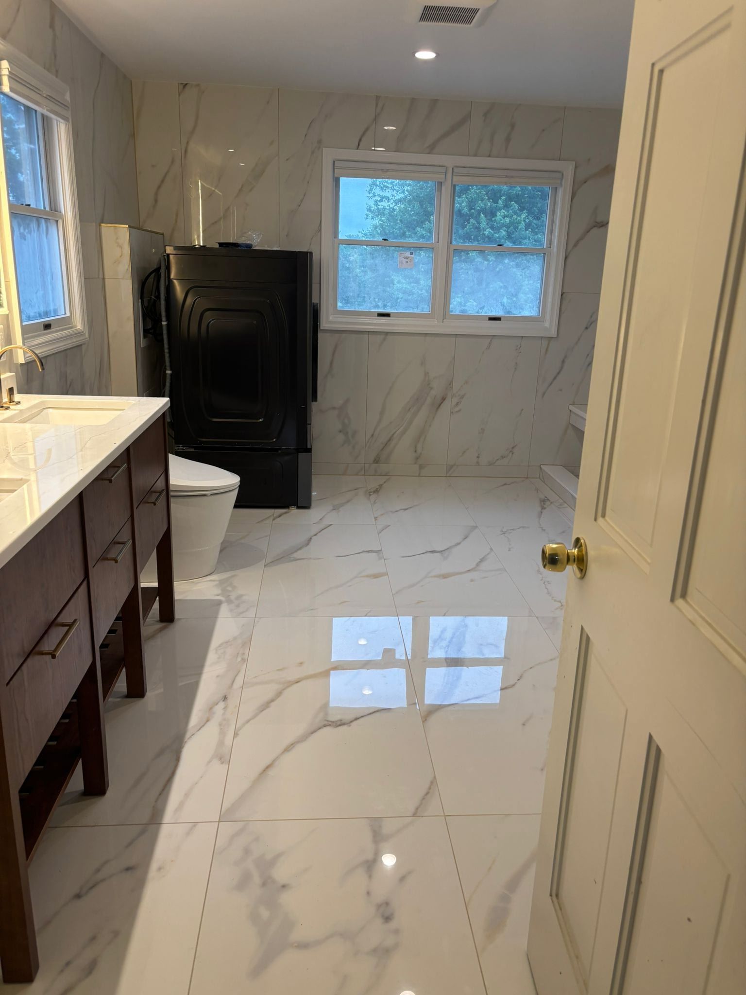 Bathroom with marble-look tile on the floor and walls. A vanity, toilet, and window are visible.