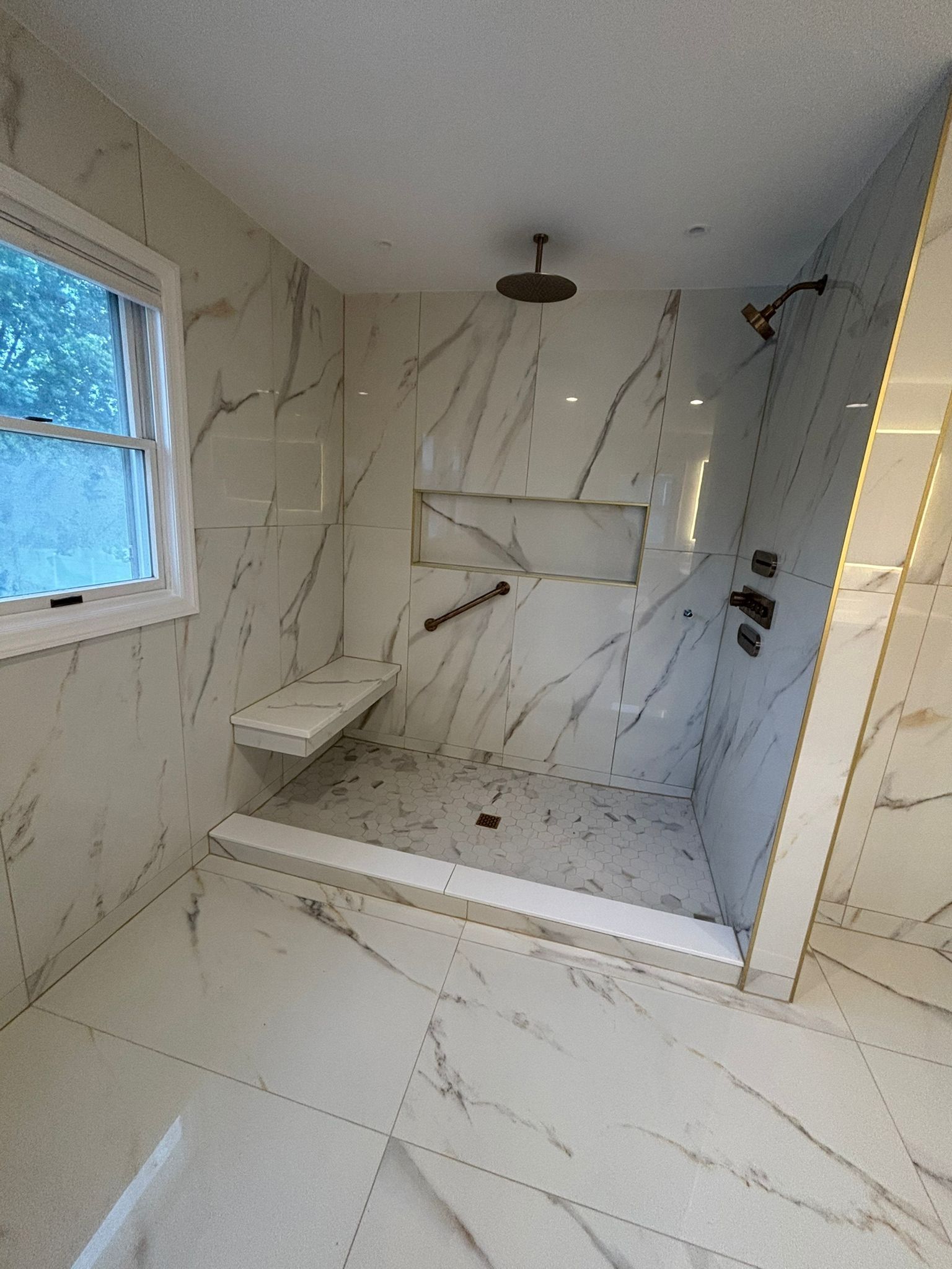 Marble-tiled shower with a bench, handrail, and rain showerhead. Includes a window.