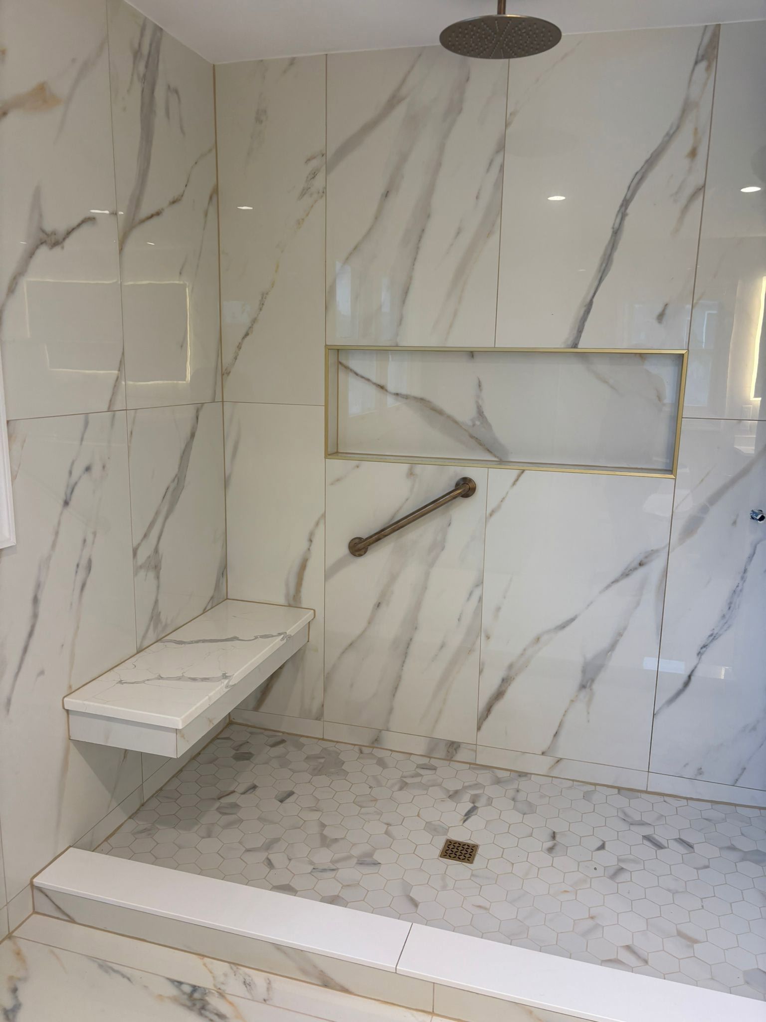 Marble-tiled shower with a built-in seat, a recessed shelf, and a grab bar for accessibility.