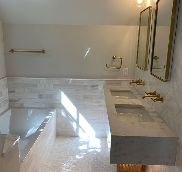 Modern bathroom with a bathtub, double sinks, gold fixtures, and marble tiles.