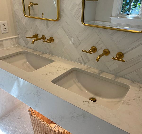 Double bathroom vanity with white sinks, marble backsplash, and gold fixtures.