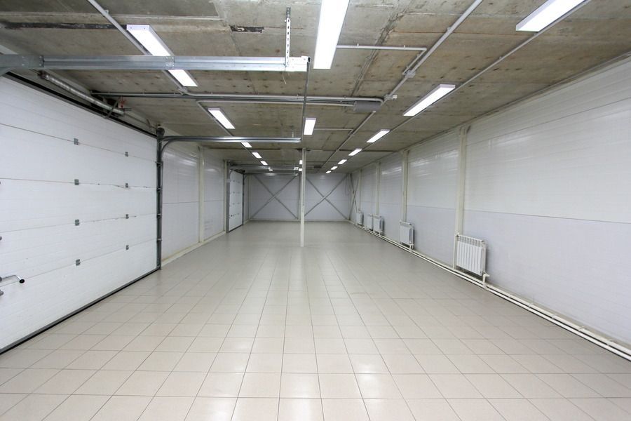 Empty white warehouse interior with a large door and ceiling lights.