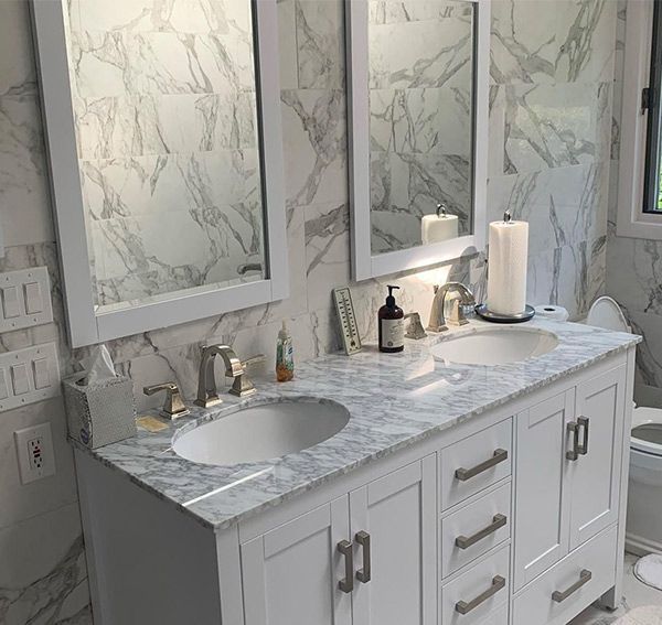 White bathroom vanity with two sinks, two mirrors, and marble-patterned walls.