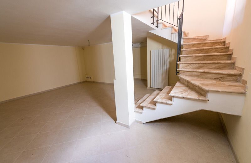 Empty room with a staircase. Beige walls and flooring. Staircase with stone steps and black railing.