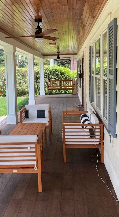 Wooden porch with seating, ceiling fans, and a view of a garden.