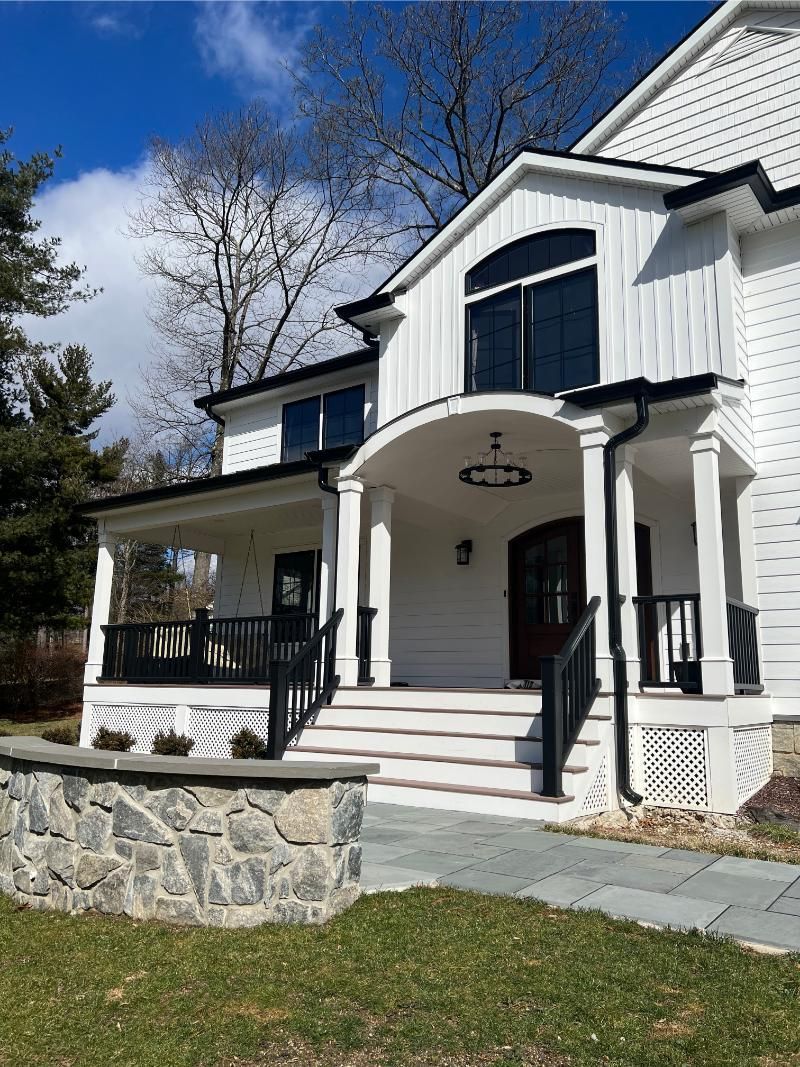 White house with black trim and a stone wall, stairs leading to the front door, blue sky.