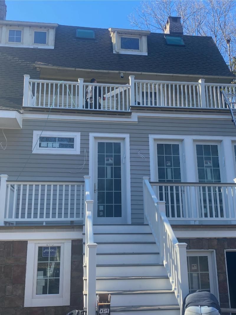 Two-story gray house with white balconies and stairs; blue sky.