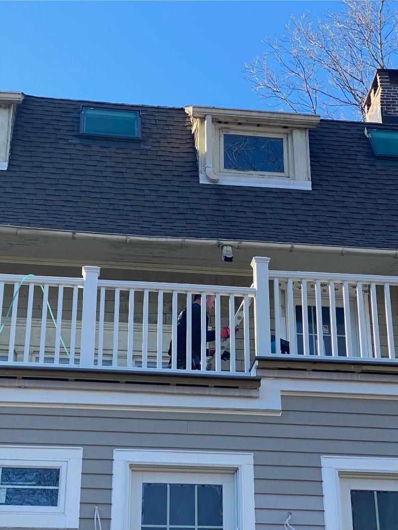 Exterior view of a multi-story building with a balcony, windows, and dormers. Gray roof and blue sky.