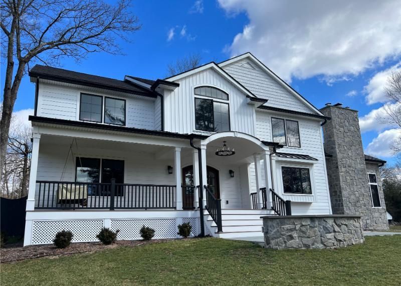 White house with black trim, a porch, and a stone chimney under a blue sky.