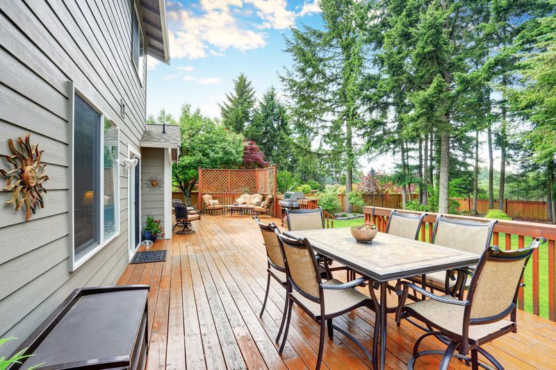 Wooden deck with dining table and chairs, overlooking a backyard with trees.