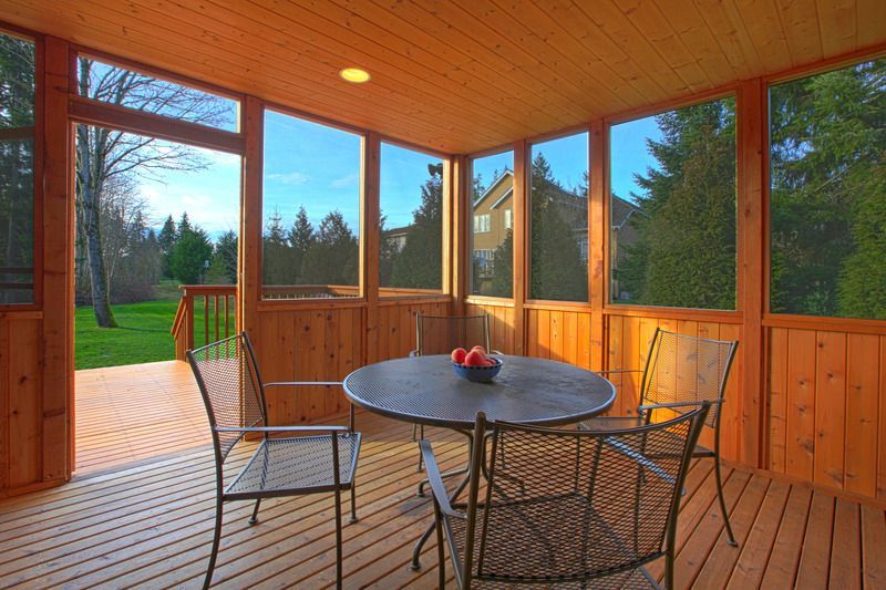 Screened-in wooden porch with round table, chairs, and view of backyard trees and a house.
