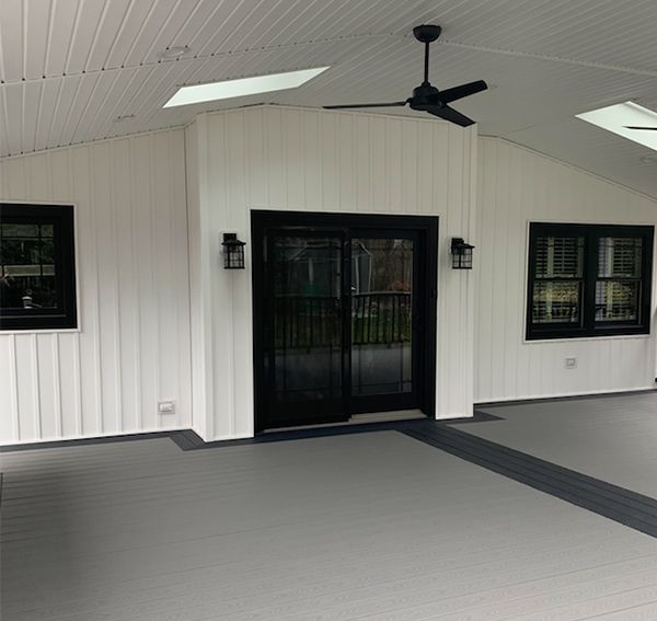Covered patio with gray floor, white walls, black sliding door, windows, and ceiling fan.