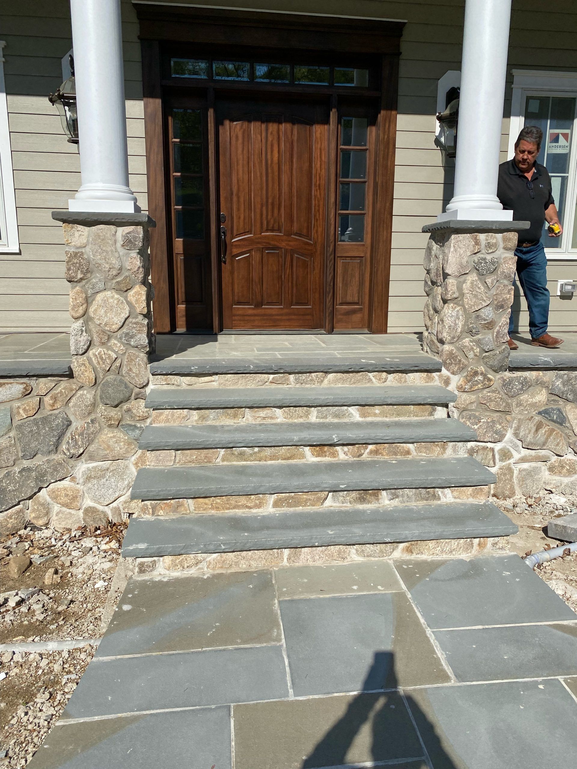 Stone steps lead to a front door with a person on the right. Columns and stone accents.