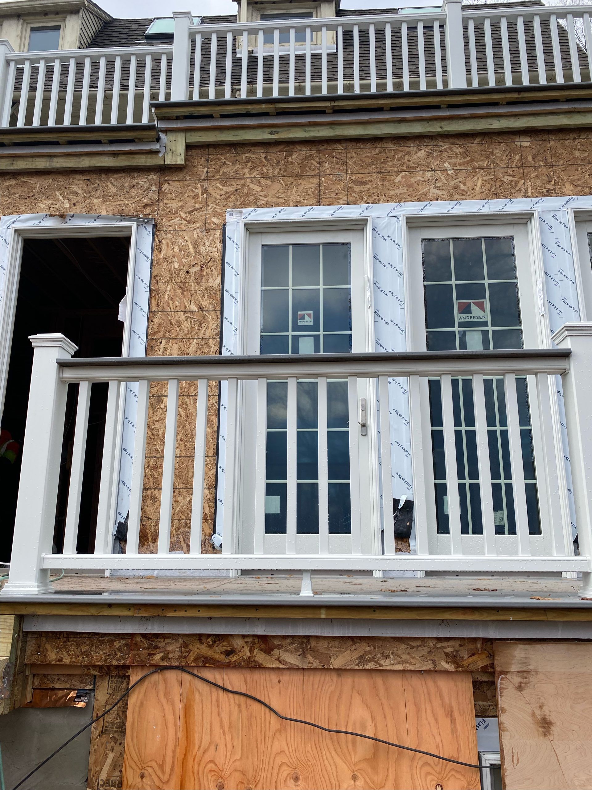 Building exterior with balcony. White railing, windows, and weathered plywood siding.