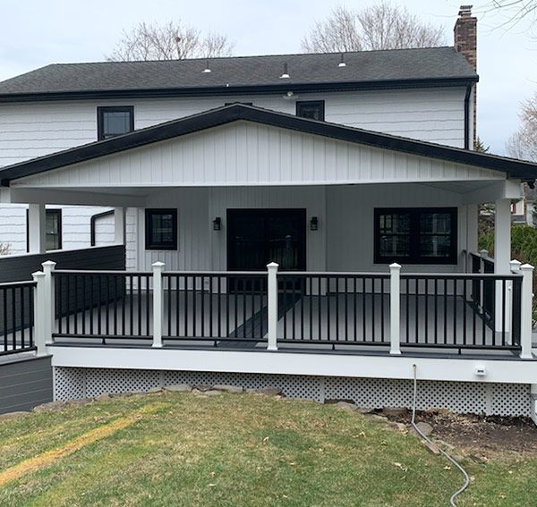White house with black trim, covered deck with black railing and gray decking.