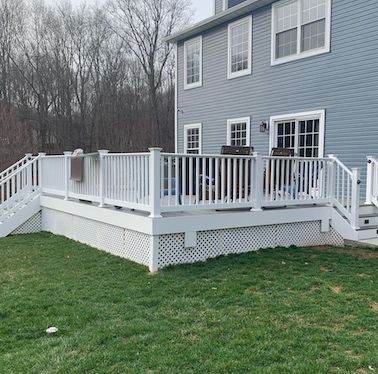 White deck attached to a gray house, with railings, stairs, and lattice skirting, set on green grass.