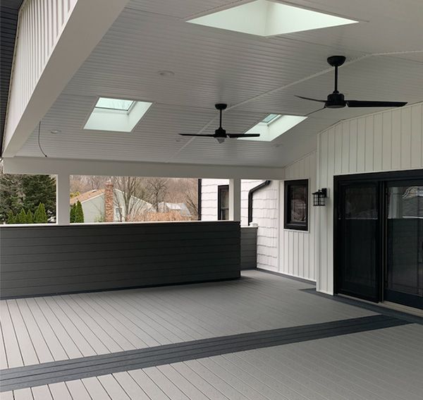 Covered porch with gray and white siding, skylights, ceiling fans, and a dark border on the deck.