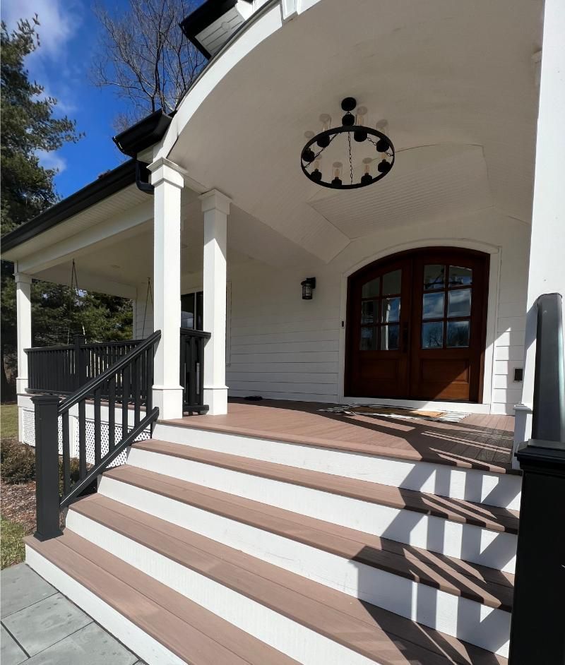 Exterior of a white house porch with brown steps, black railings, and a clock hanging from the ceiling.