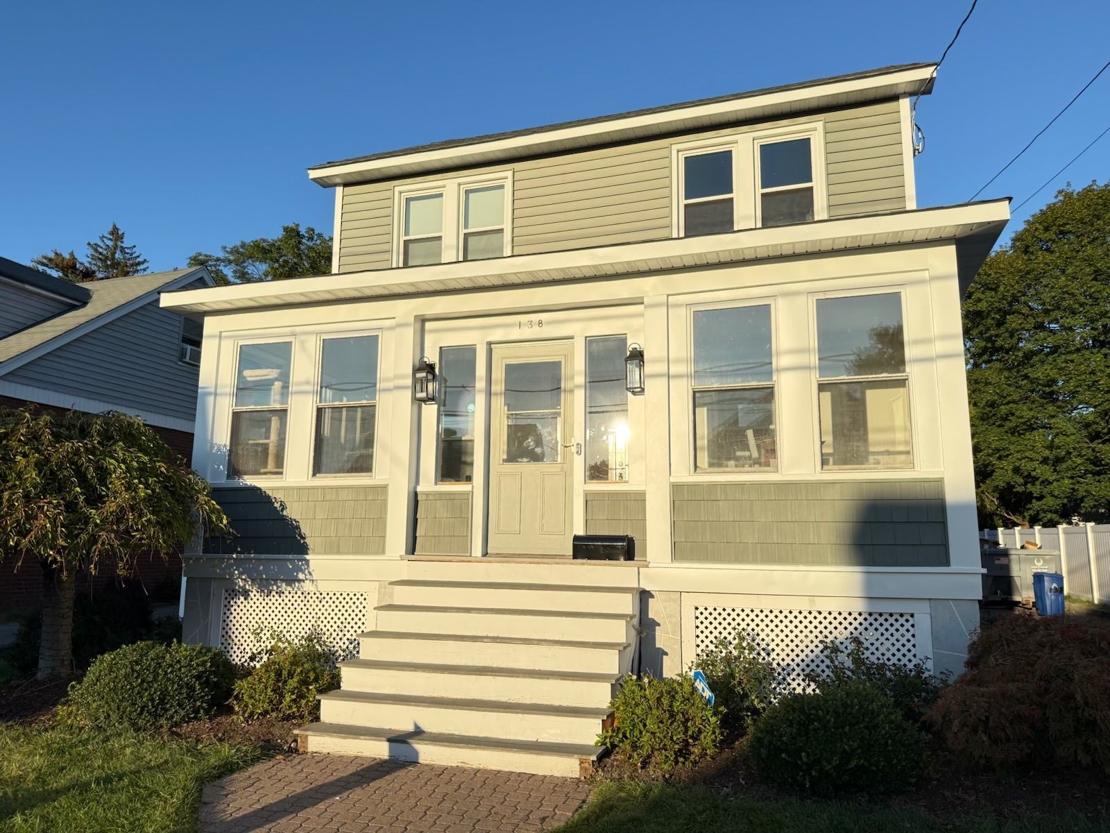 Two-story house with light gray siding, white trim, and a small porch. Bright sunlight.