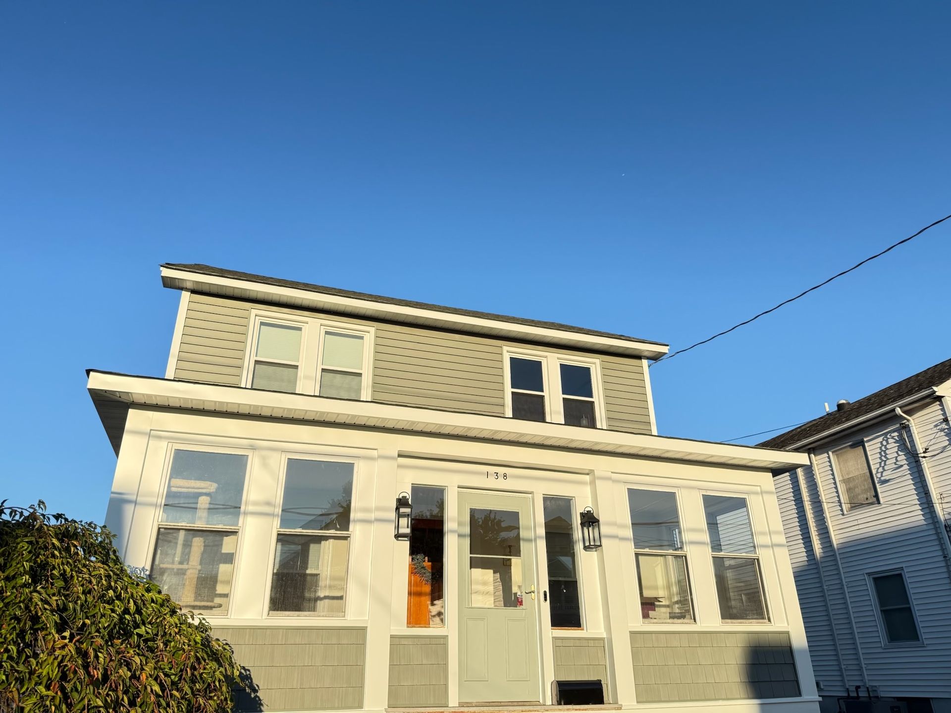 Two-story house with light gray siding, glass windows, and a blue sky.