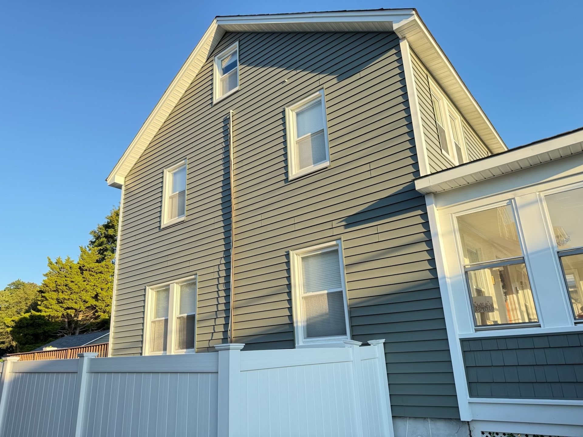 Gray house with a perforated siding, windows, and white trim against a blue sky.