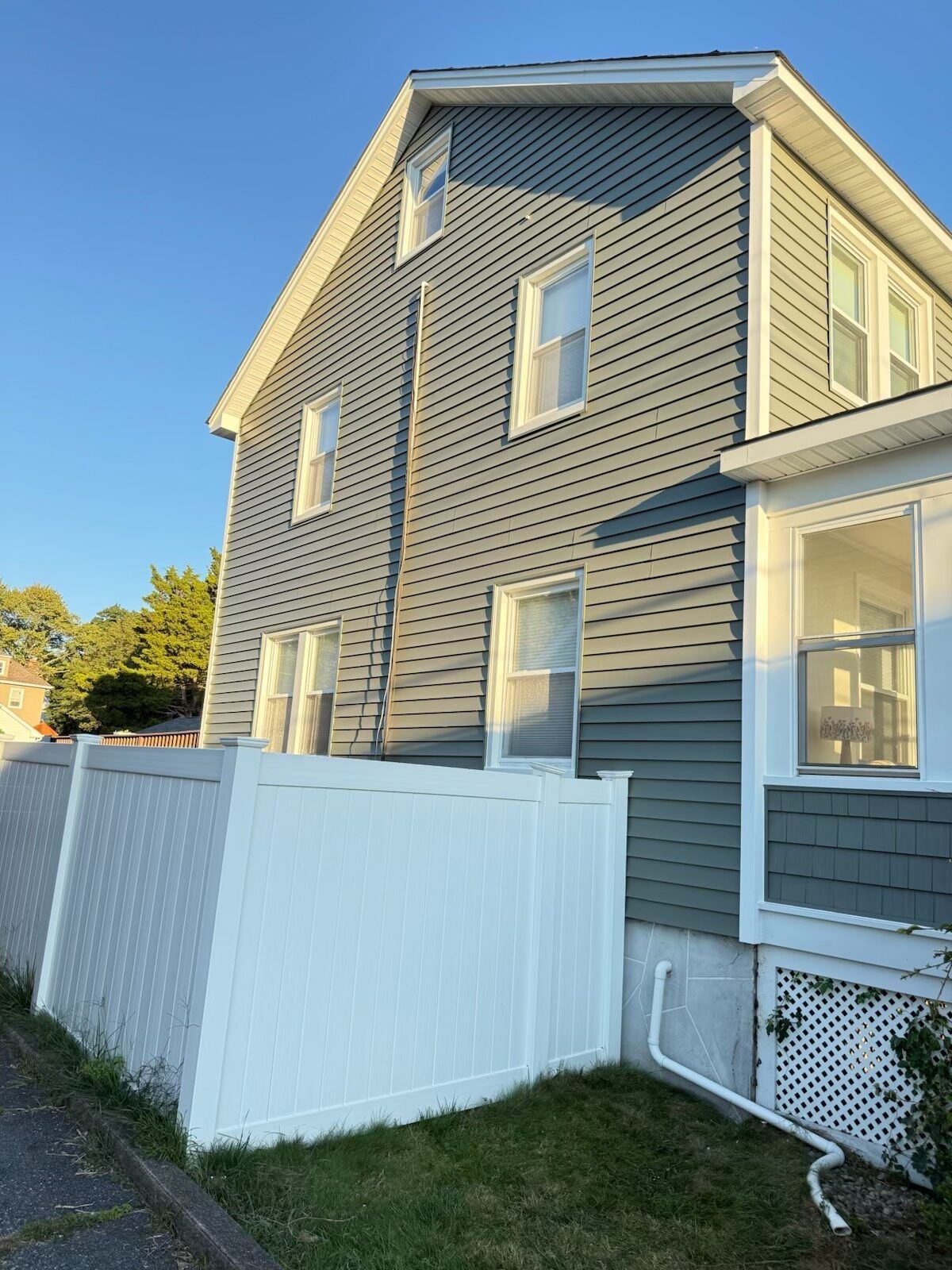 Gray house with white trim and fence. Sunlight on the side of the building.